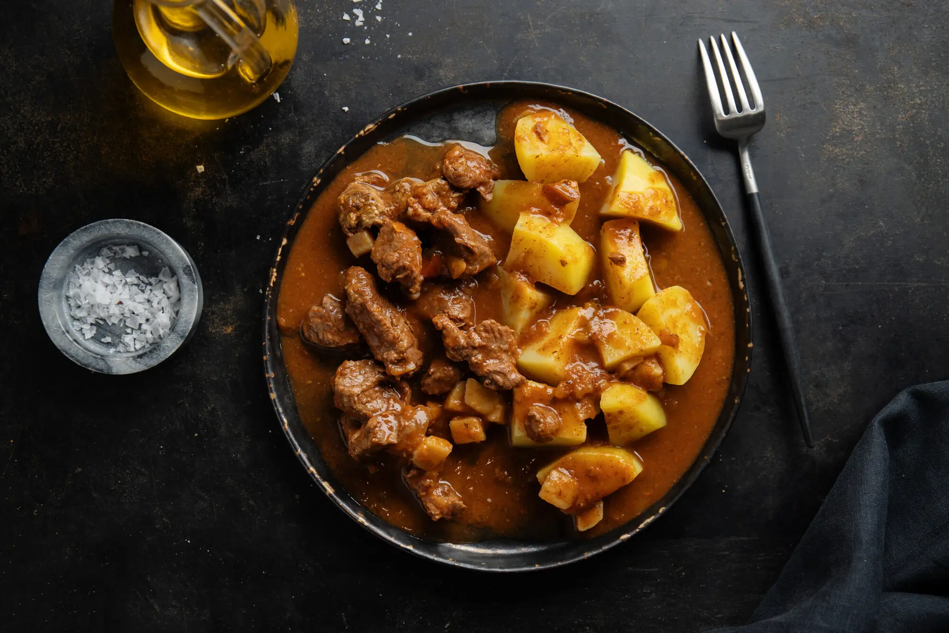 Beef braised with potatoes in a deep brown sauce, served in a dark dish